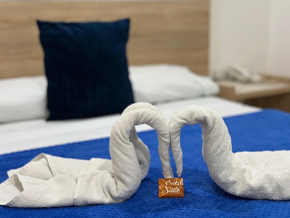 A bed with a blue blanket, a white pillow, and a dark blue pillow. There is a small brown tag on the blanket.