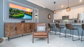 A modern kitchen with white cabinets, a stainless steel refrigerator, and a bar area with stools. - Amazing Disney resort style & FREE Waterpark 2481 (Kissimmee)