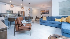 A modern kitchen with stainless steel appliances, a dining area with a blue sofa and a coffee table, and a ceiling fan. - Amazing Disney resort style & FREE Waterpark 2481 (Kissimmee)