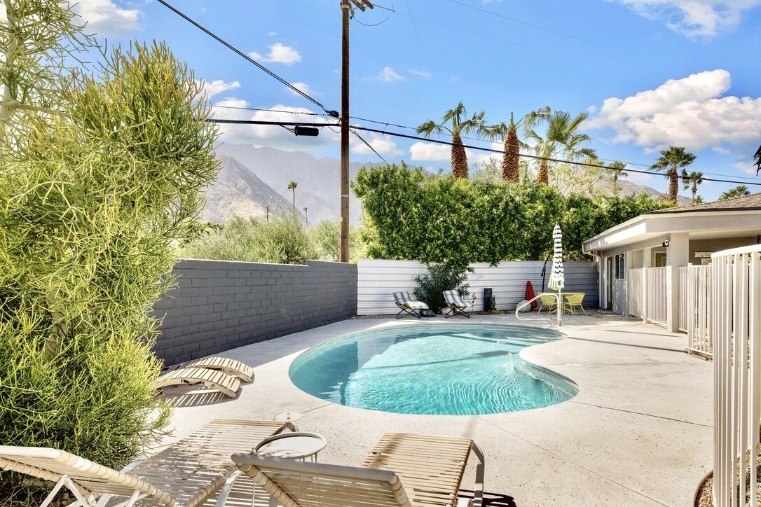 A backyard with a swimming pool, lounge chairs, and a view of mountains.