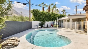 A swimming pool with lounge chairs, a white fence, and a building with a porch. - Perfect Palm Springs Studio Retreat Near Downtown!
 (Palm Springs)