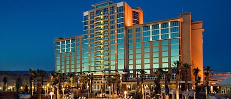 A large hotel with multiple floors, a swimming pool, and palm trees.