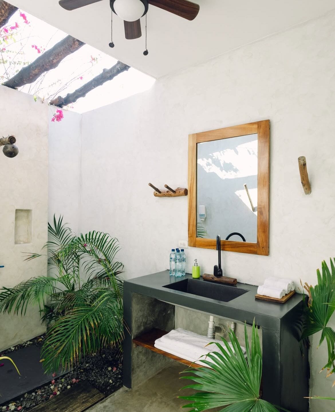 A modern bathroom with a large mirror, a dark sink, and a ceiling fan.