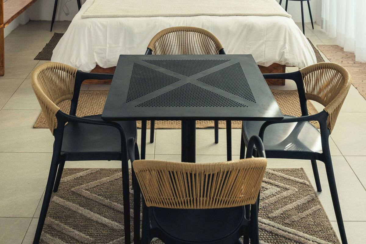 A bedroom with a bed, two bedside tables, a table with chairs, and a rug.
