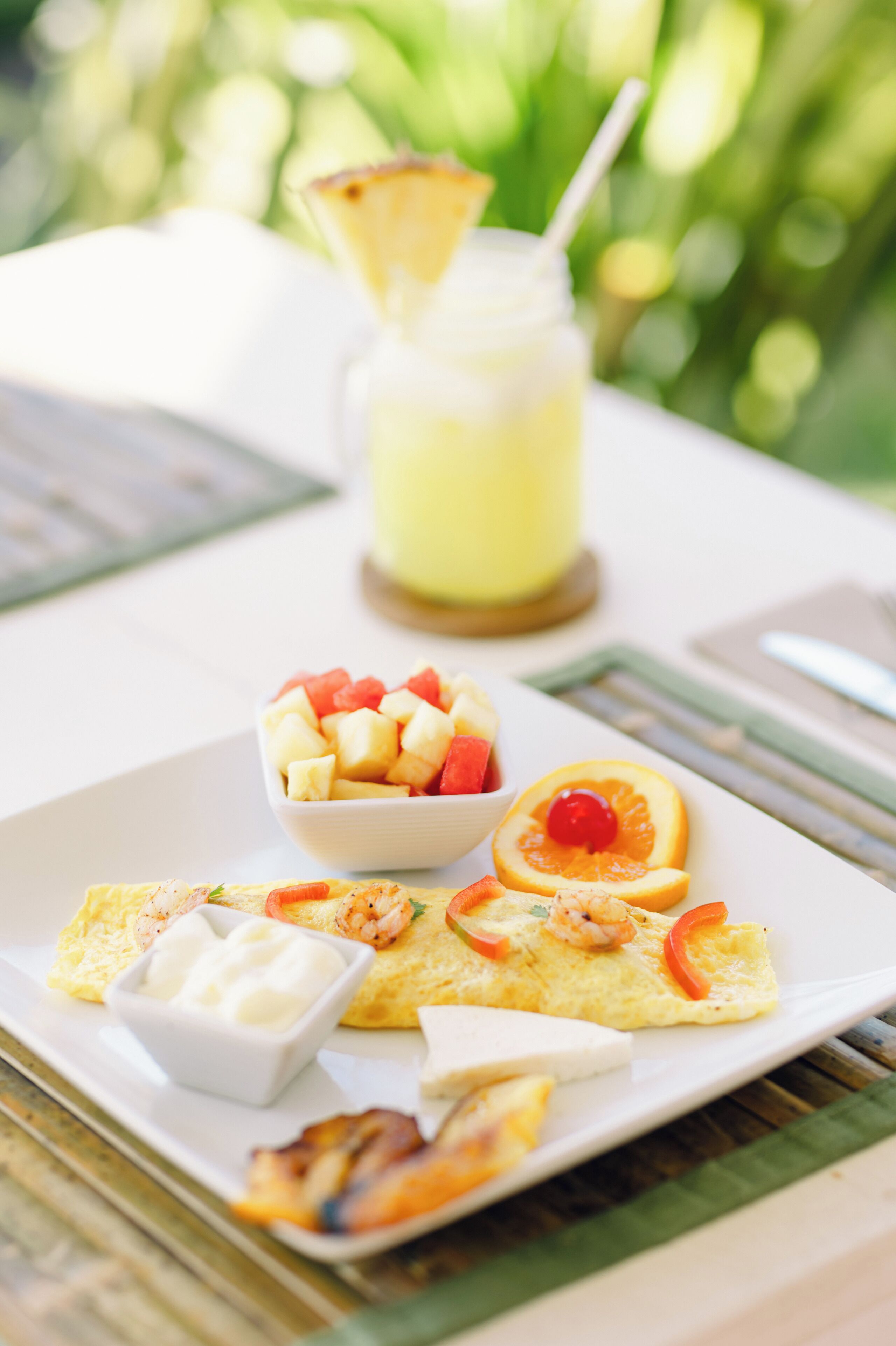 Une assiette de petit-déjeuner avec des fruits, des crevettes et des toasts, et un verre de boisson sur une table.