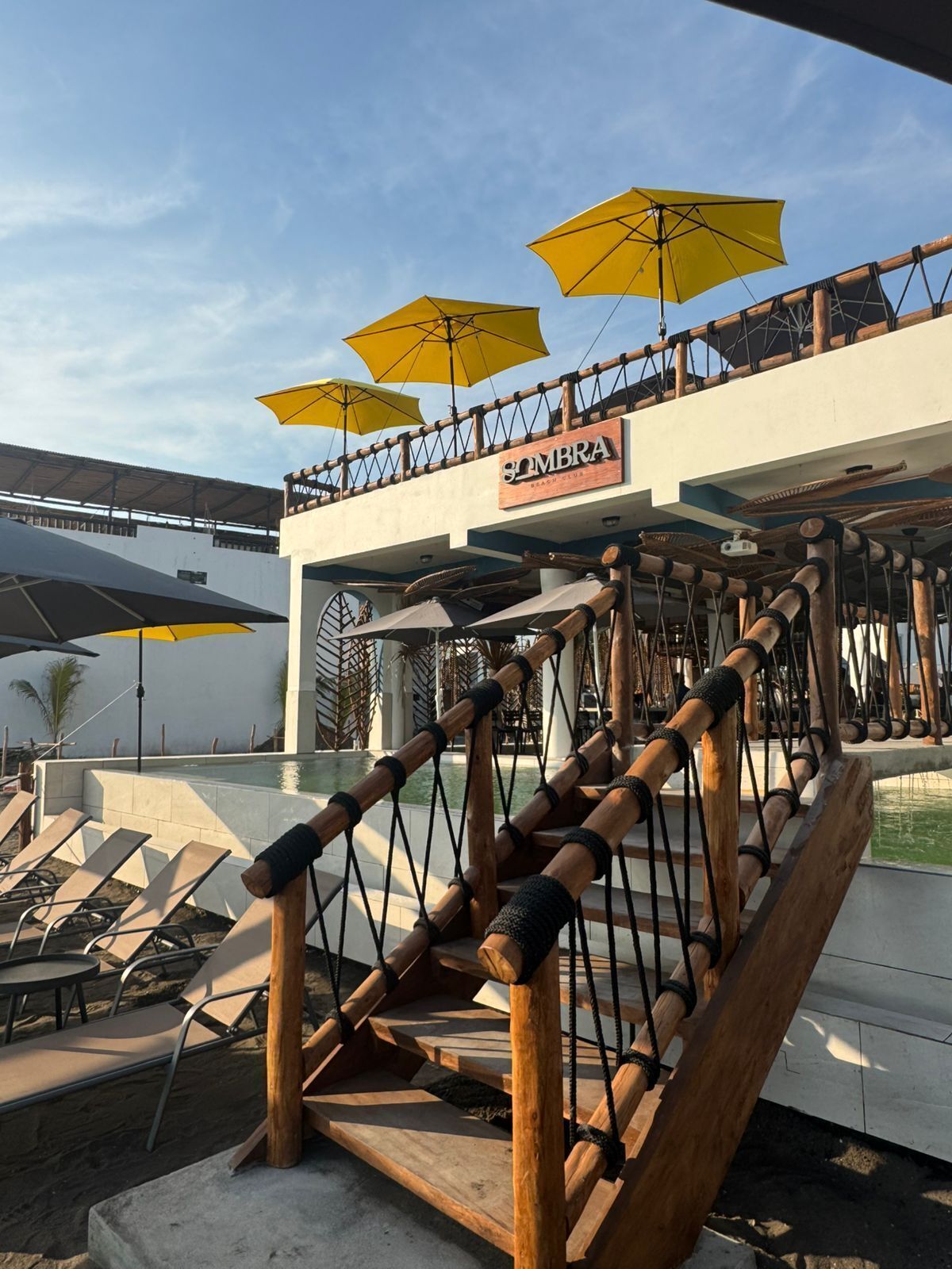 Une terrasse en bois sur laquelle est fixée une enseigne indiquant « SOMBRA BEACH CLUB ».