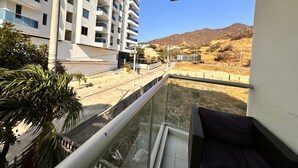 A balcony with a view of a multi-story building, a road, and a hilly landscape. - SGH Hotel Rodadero Suites (Santa Marta)