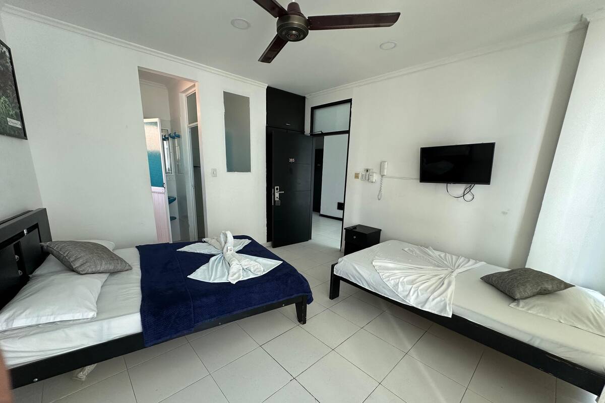 Ein Hotelzimmer mit zwei Betten, einem Deckenventilator, einem Fernseher und einer Tür zu einem Badezimmer.