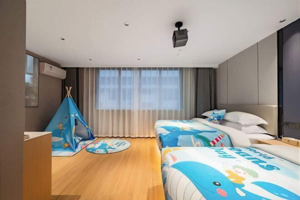 Ett hotellrum med en säng, ett skrivbord, ett fönster med gardiner, ett tält och en projektor i taket.