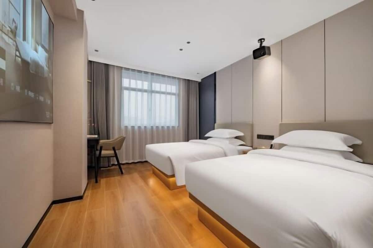 Ett hotellrum med två sängar, ett skrivbord och ett stort fönster med gardiner.