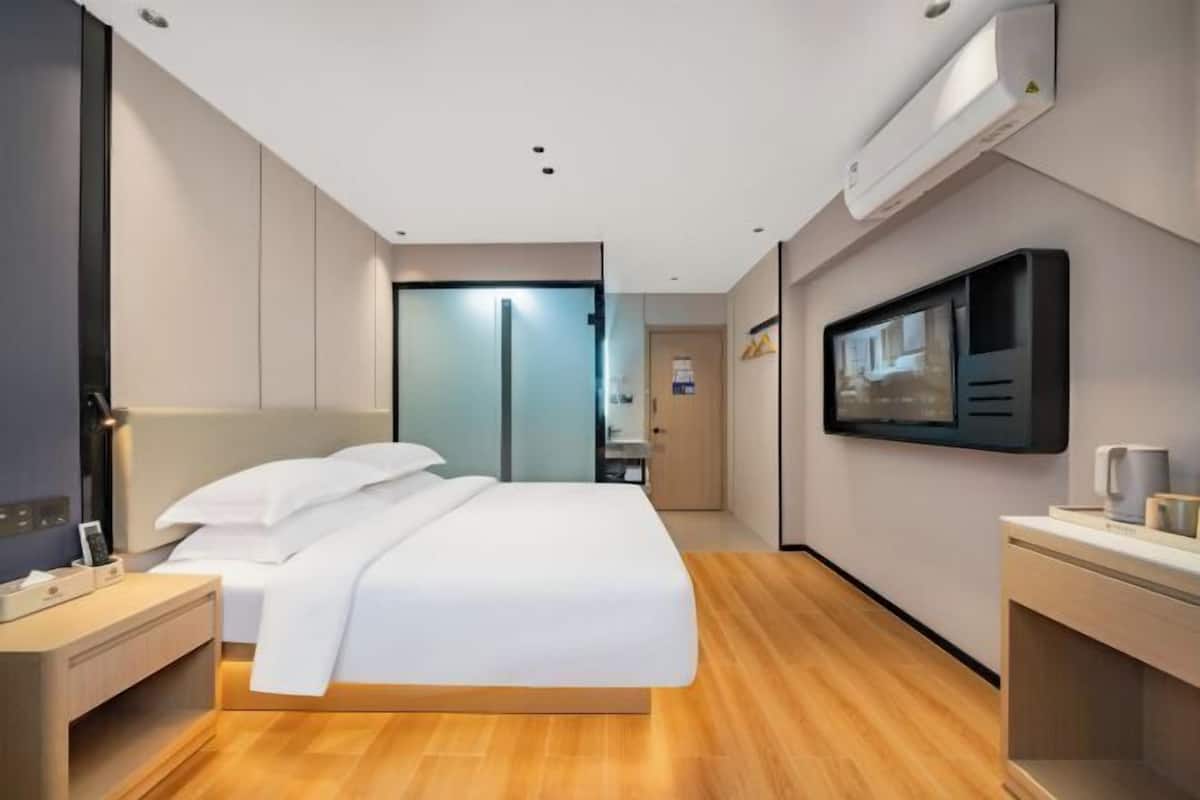 Ett modernt hotellrum med en säng, ett sängbord, en TV och en väggmonterad luftkonditioneringsanläggning.