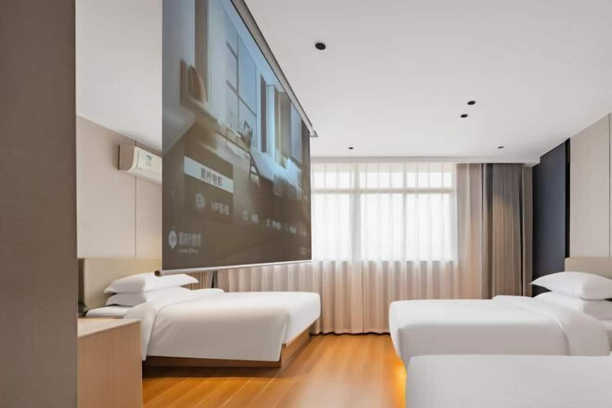 Ett hotellrum med två sängar, ett stort fönster med gardiner och en projektionsduk på väggen.