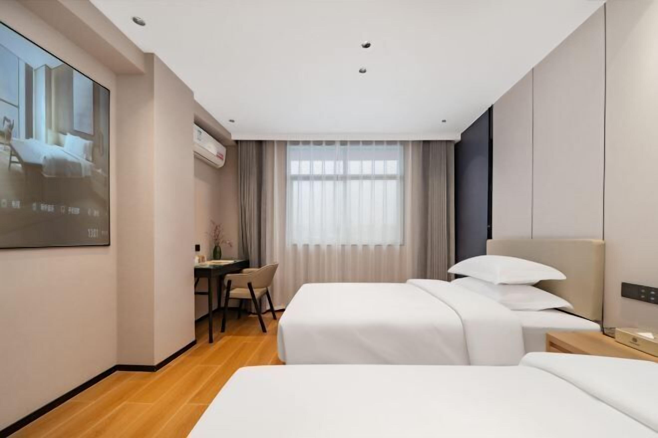 Una habitación de hotel con dos camas, un escritorio y un amplio ventanal con cortinas.