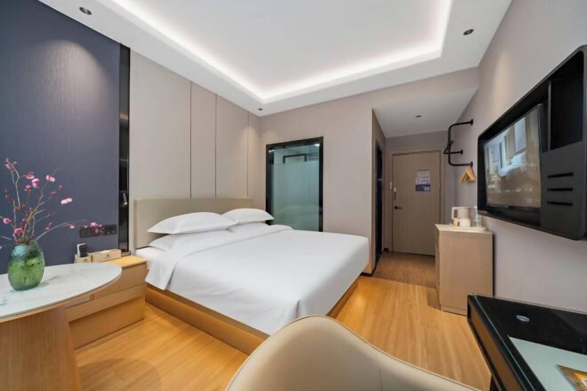 Ett modernt hotellrum med en säng, ett nattduksbord, en TV och ett skrivbord med en stol.