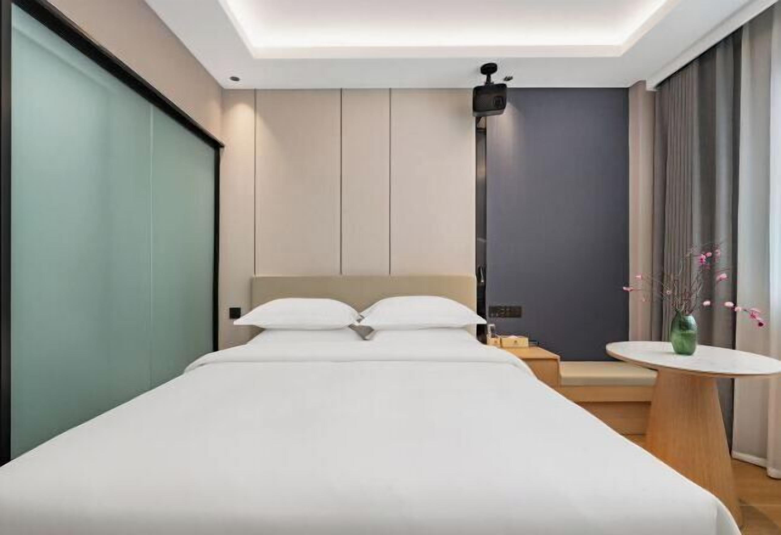 Ein modernes Hotelzimmer mit einem großen Bett, einer kleinen Sitzecke, einem runden Tisch und einer Deckenleuchte.