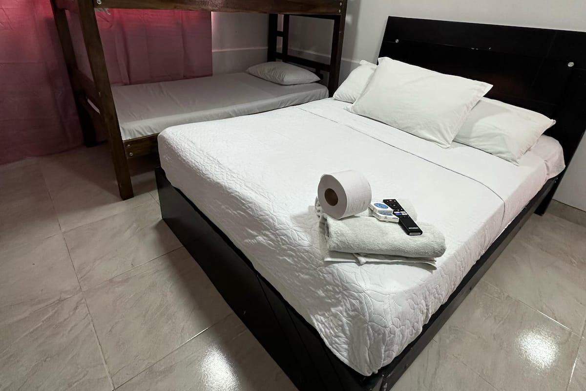 A bunk bed room with a single bed, a remote control, and a roll of toilet paper on the bed.