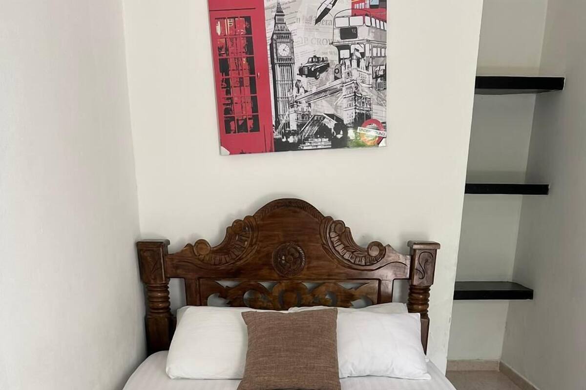 A neatly made bed with a patterned bedspread, pillows, and a remote control on the side.