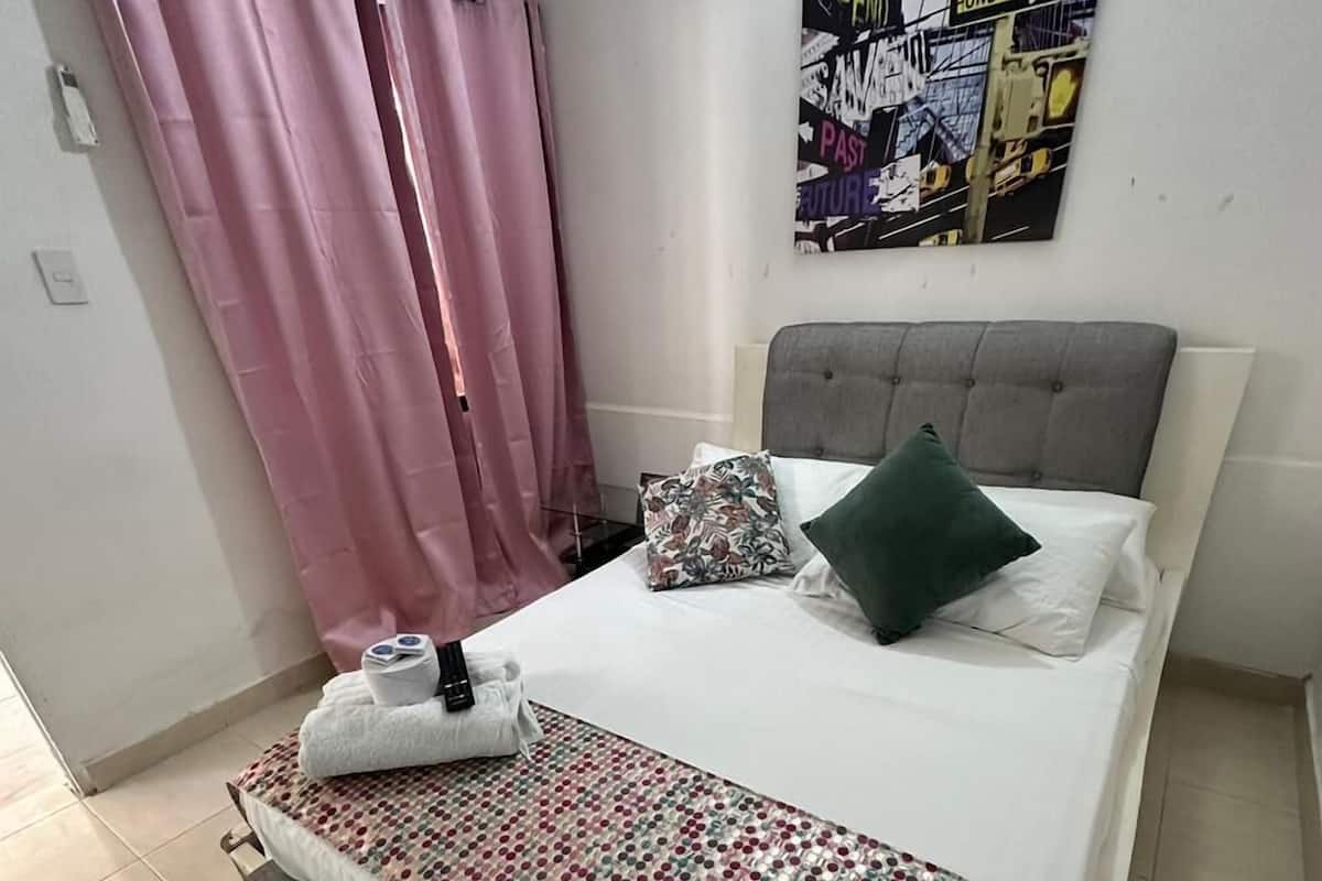 A bedroom with a bed, pillows, a blanket, a headboard, a wall-mounted air conditioner, and a poster.