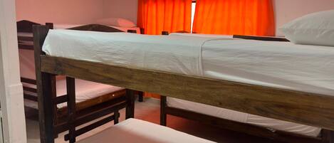 A dormitory room with bunk beds, a window with orange curtains, and a white wall.