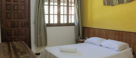 Um quarto com uma cama, uma escrivaninha de madeira, uma janela com cortinas e uma decoração de peixe na parede.