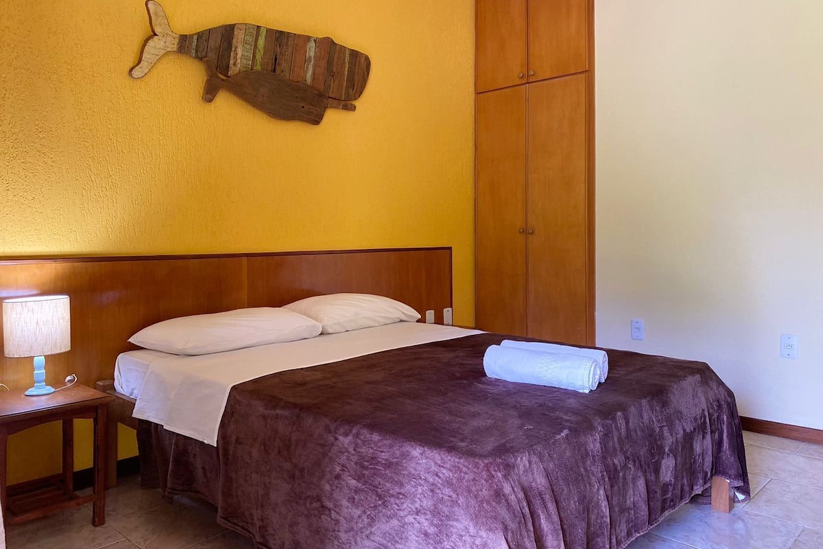 A bedroom with a wooden headboard, a bed with a brown bedspread, a nightstand with a lamp, and a wooden wardrobe.
