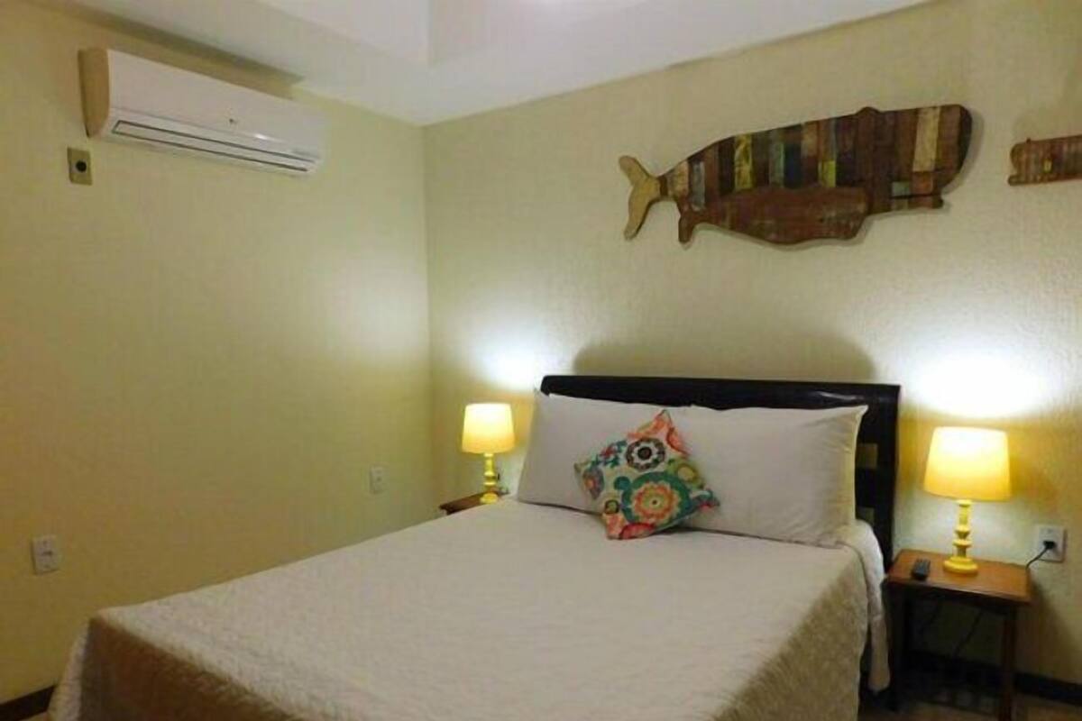 A hotel room with a bed, two bedside tables with lamps, a wall-mounted air conditioner, and a decorative fish sculpture.