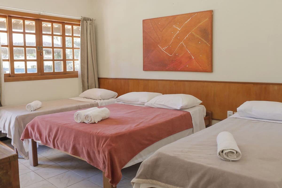 A hotel room with two beds, each with a rolled towel, a wooden headboard, and a window with curtains.