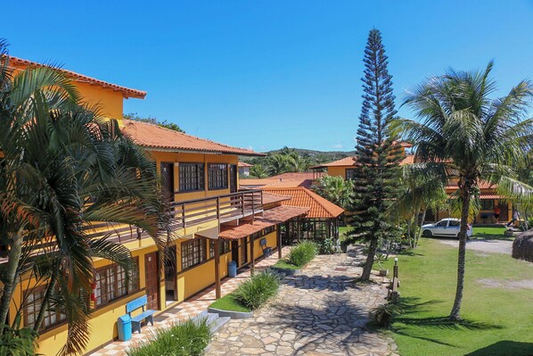 A yellow building with a red roof, a stone pathway, and palm trees. - POUSADA ELOHIM DE BUZIOS (Búzios)