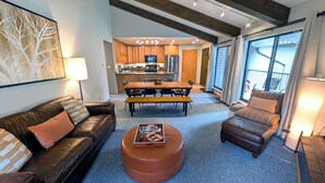 A modern living room with a leather sofa, a round ottoman, and a dining area with a wooden table and chairs. - Remodeled Condo w/ FREE WiFi, Parking, Heated Pool, Hot Tubs, Skier Shuttle (Avon)