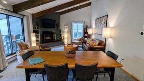 A spacious living room with a large wooden table, leather chairs, a fireplace, a television, and a bookshelf. - Remodeled Condo w/ FREE WiFi, Parking, Heated Pool, Hot Tubs, Skier Shuttle (Avon)
