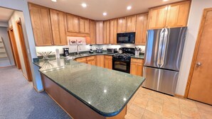 A kitchen with wooden cabinets, a stainless steel refrigerator, a microwave, and a granite countertop. - Remodeled Condo w/ FREE WiFi, Parking, Heated Pool, Hot Tubs, Skier Shuttle (Avon)