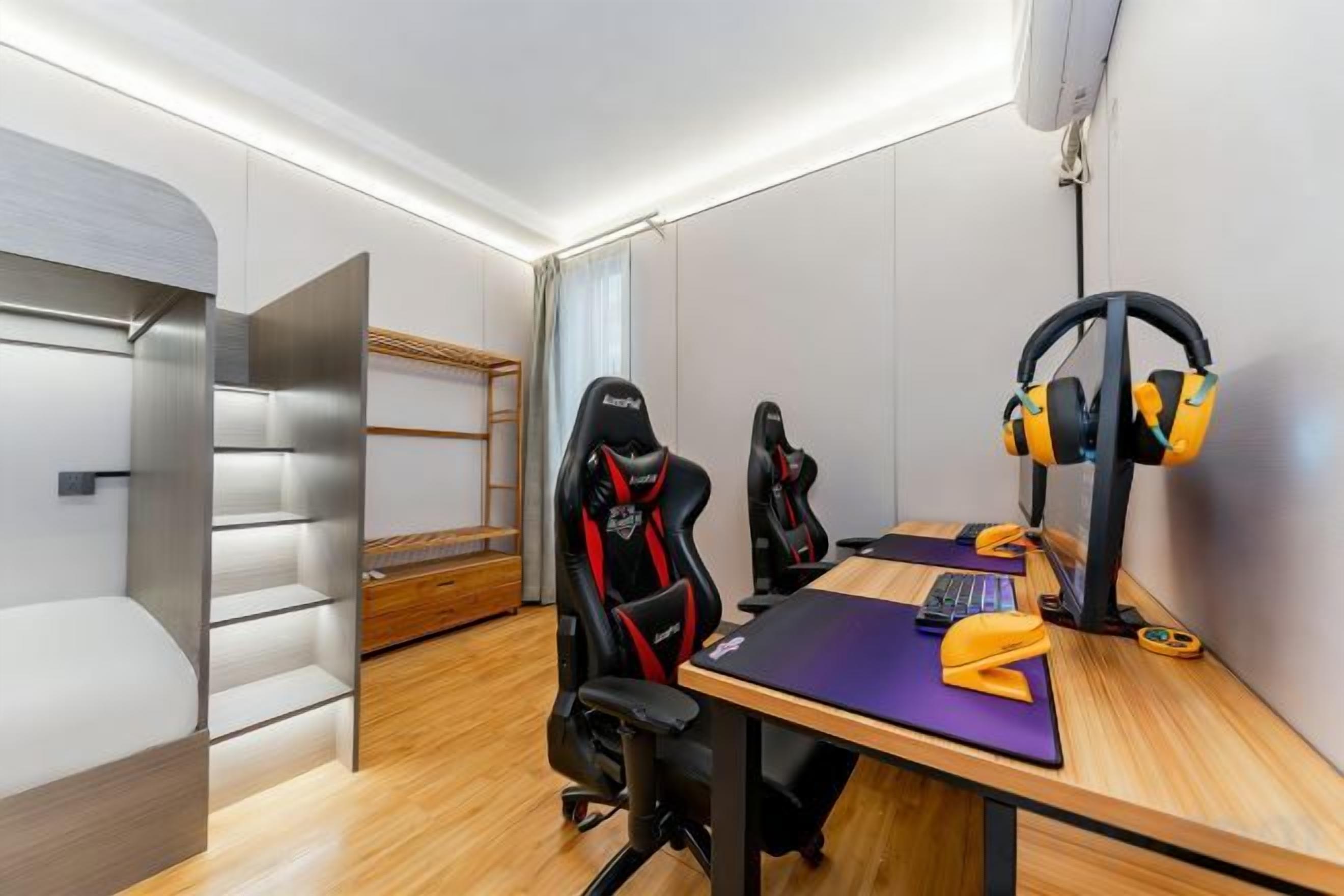 Ein Zimmer mit einem Etagenbett, zwei Gaming-Stühlen, einem Schreibtisch inklusive Tastatur und Kopfhörern auf einem Ständer.