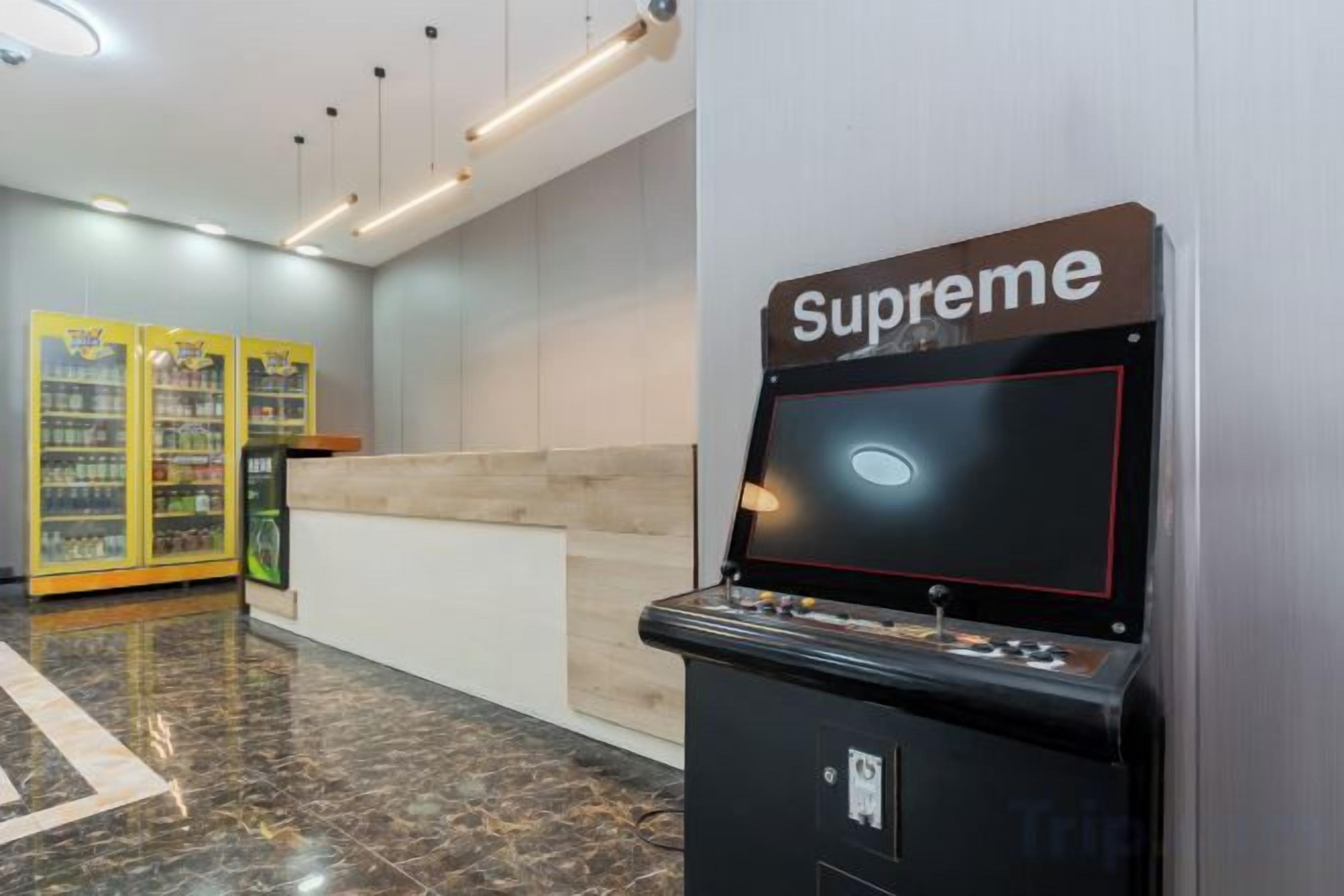A gaming machine labeled 'Supreme' in a lobby area with a reception desk and vending machines in the background.
