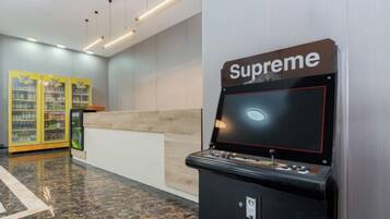 A gaming machine labeled 'Supreme' in a lobby area with a reception desk and vending machines in the background.