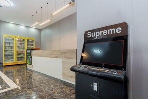 A gaming machine labeled 'Supreme' in a lobby area with a reception desk and vending machines in the background. - Aoyou Esports Hotel (Shanghai Lujiazui) (Shanghai)