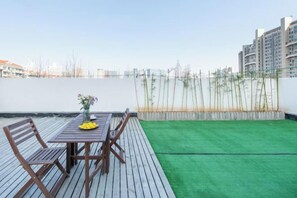 A rooftop terrace with a wooden table and chairs, a small vase with flowers, and a view of a body of water and buildings in the distance. - Aoyou Esports Hotel (Shanghai Lujiazui) (Shanghai)