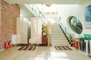 A modern hotel lobby with a staircase, a brick wall, and a view of the upper floor. - Aoyou Esports Hotel (Shanghai Lujiazui) (Shanghai)