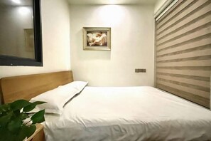 A bedroom with a bed, a nightstand, a potted plant, a framed artwork on the wall, and a window with blinds. - Aoyou Esports Hotel (Shanghai Lujiazui) (Shanghai)