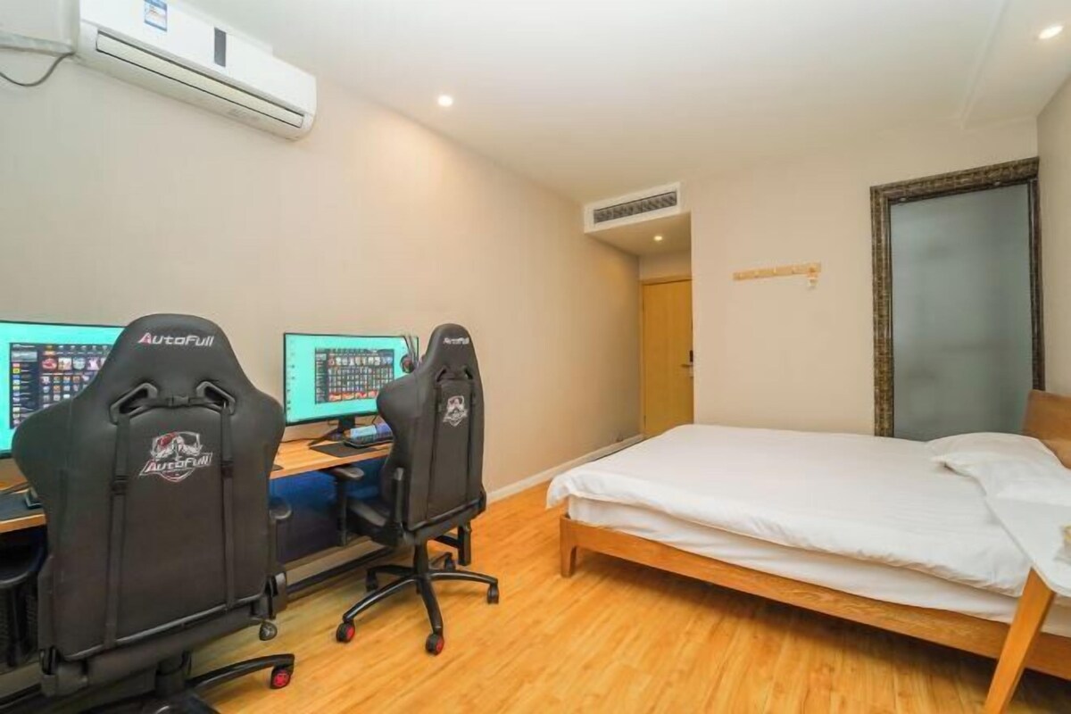 A room with a bed, two gaming chairs, two monitors, and a wooden floor.