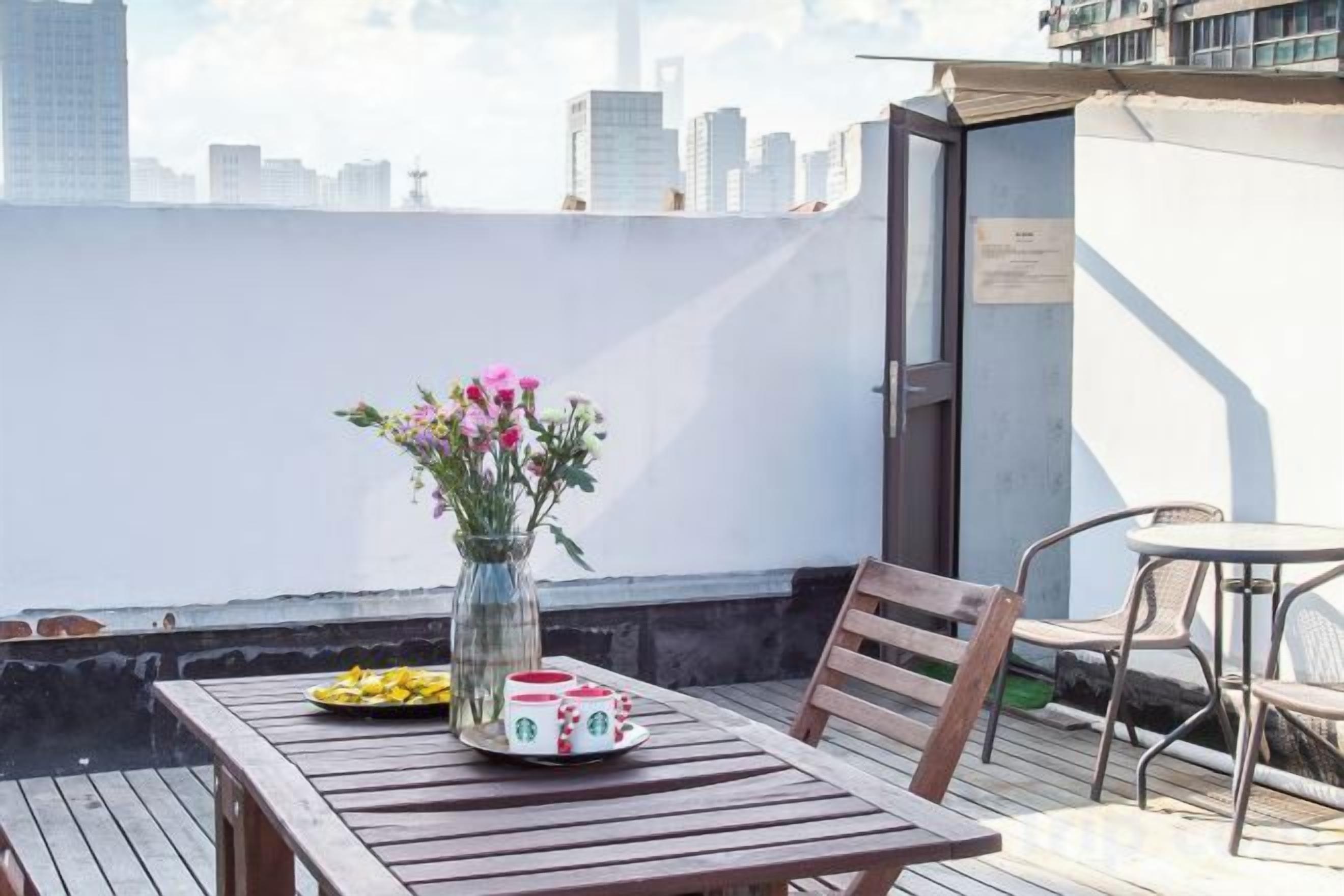 En tagterrasse med et bord, stole, en blomstervase og udsigt over byens skyline.