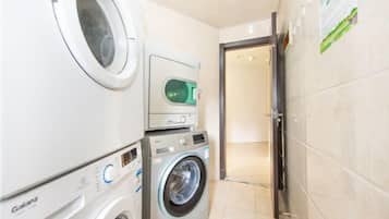 Uma lavanderia com máquina de lavar e secar de carregamento frontal, secadora de parede e uma porta que dá para outro cômodo.
