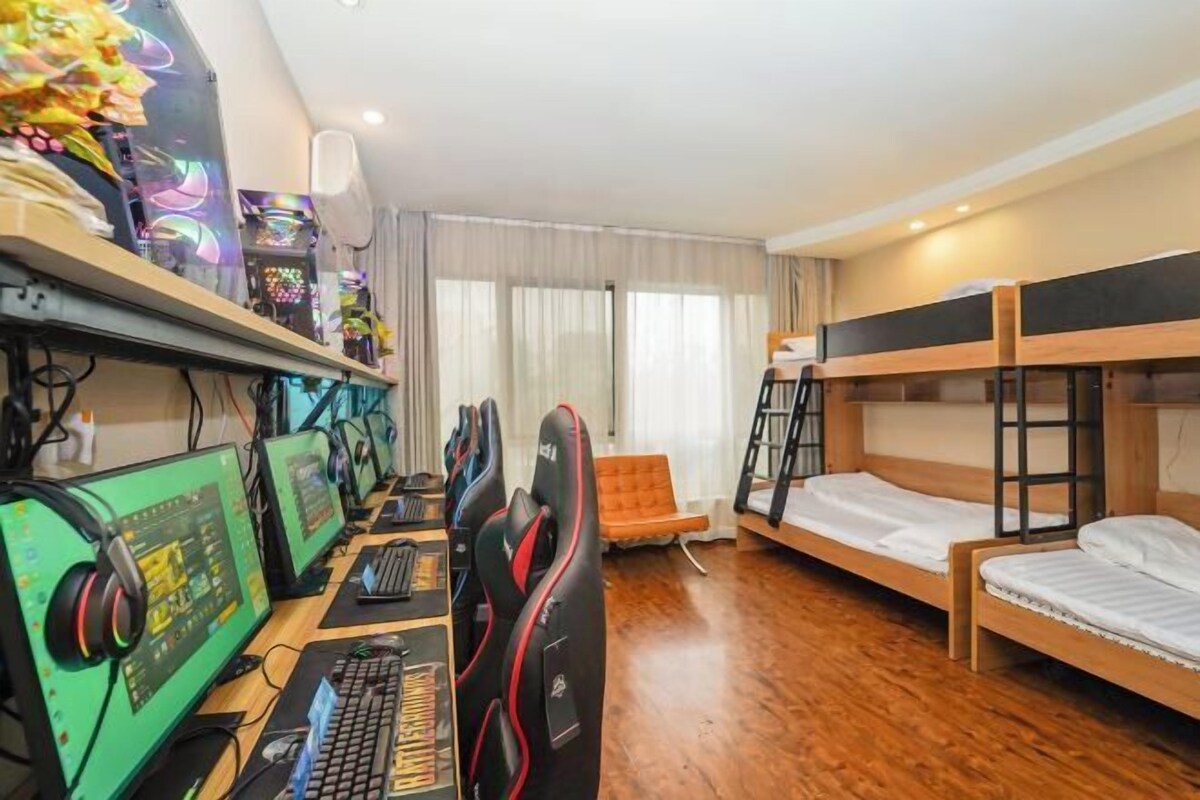 A room with a gaming setup, bunk beds, and a window with curtains.