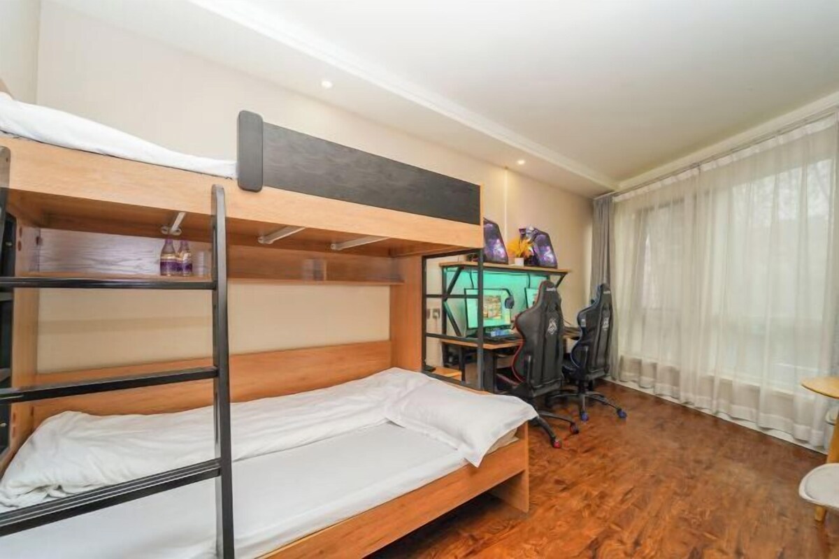 A bunk bed room with a desk and chair, a small table, and a window with curtains.