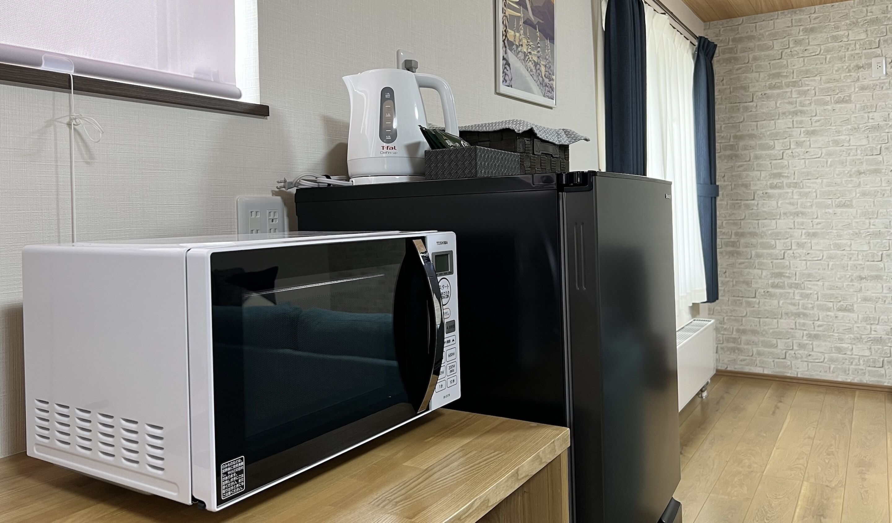 Cocina compacta con microondas, refrigerador y hervidor sobre una encimera de madera.