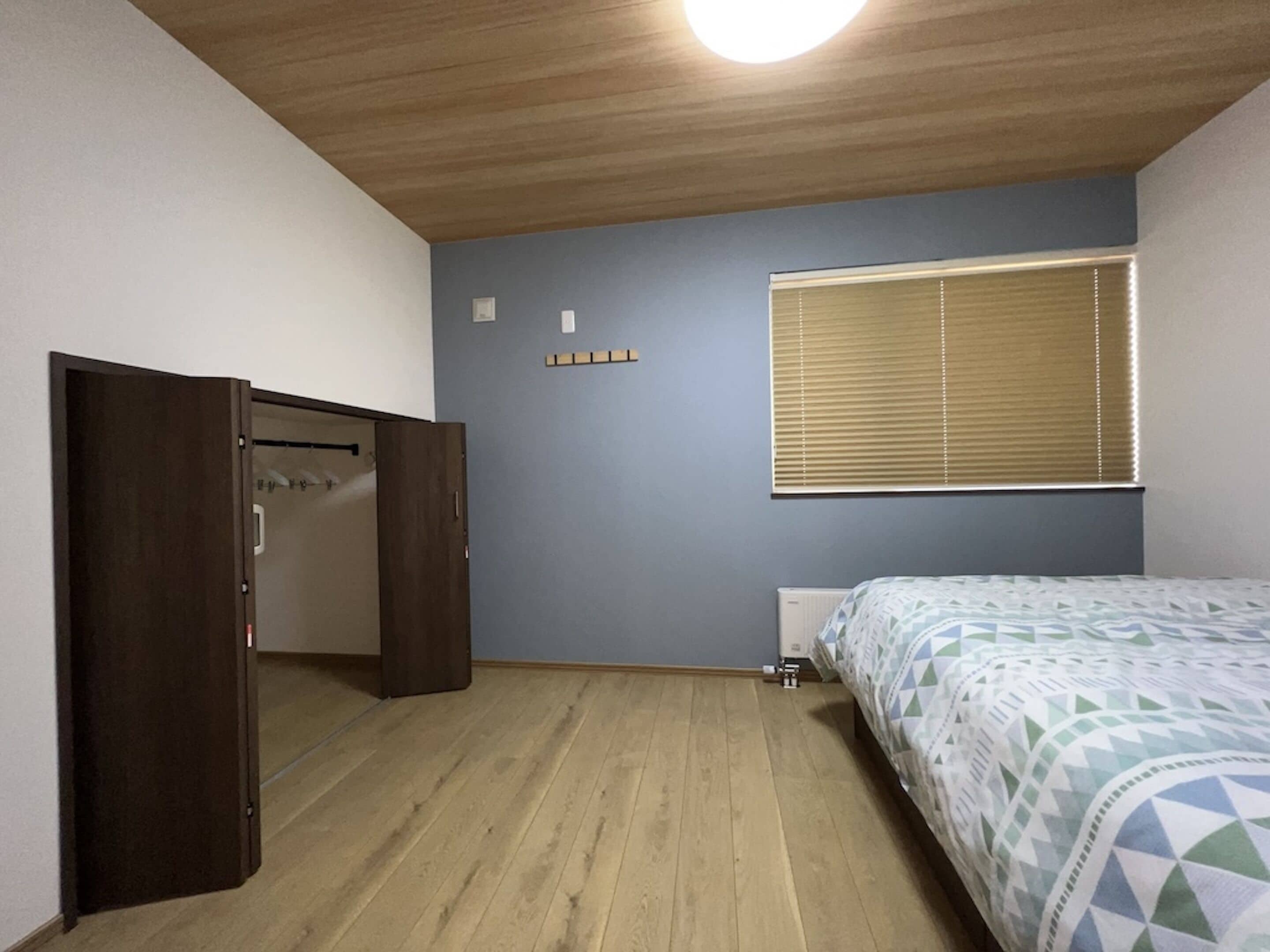 A bedroom with a bed, a wardrobe, a window with blinds, and a radiator.