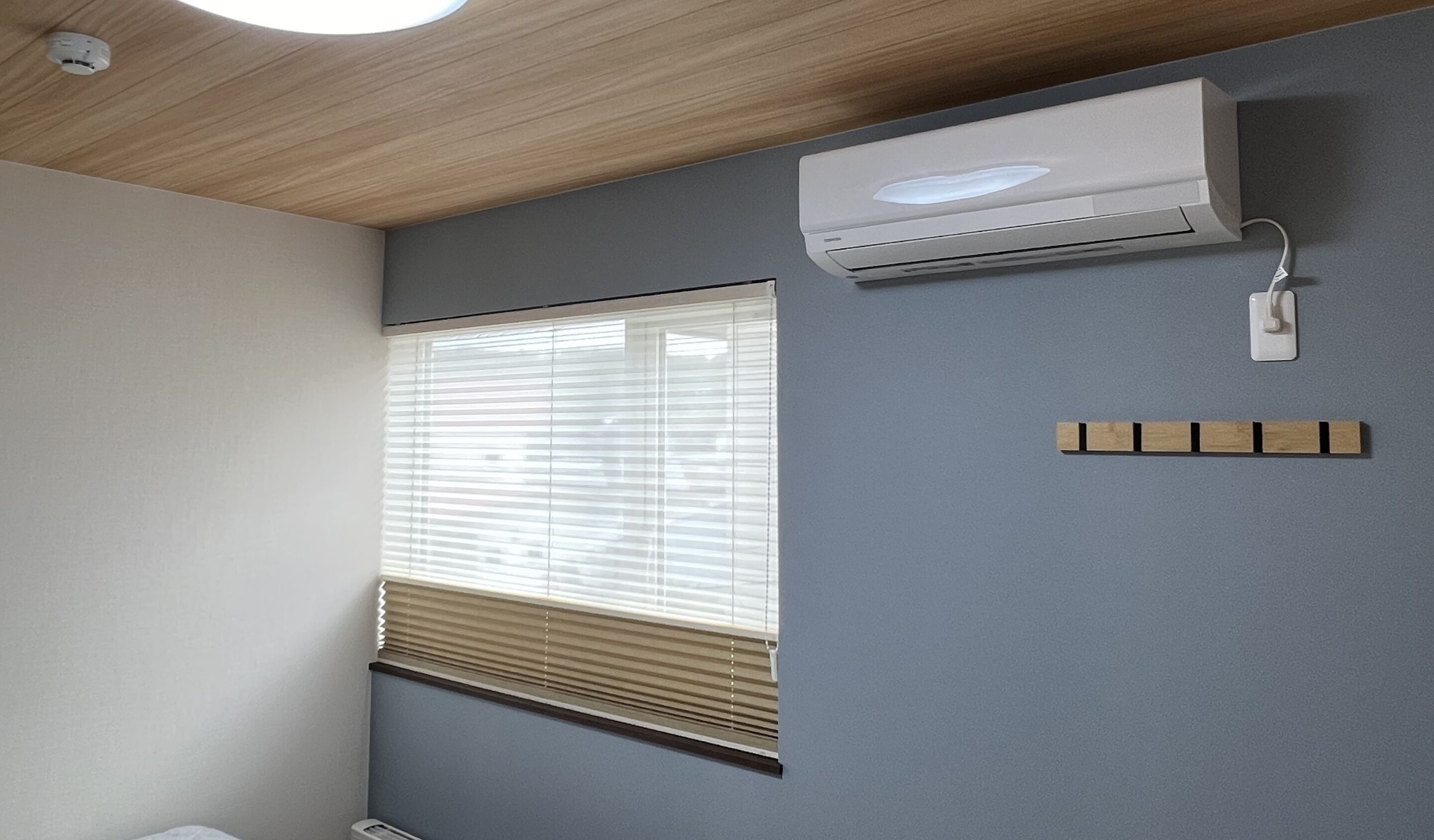 A room with a window, an air conditioning unit, and a power outlet on the wall.