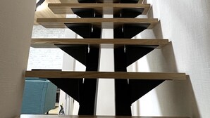 Een moderne trap met houten treden en metalen leuningen, leidend naar een plateau met een rood bord met daarop een nooduitgang.'