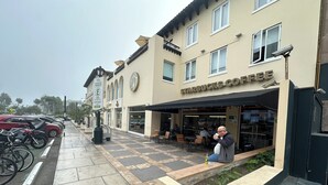 A Starbucks with outdoor seating, a parking area with cars and a covered bike rack, and a pedestrian walkway.