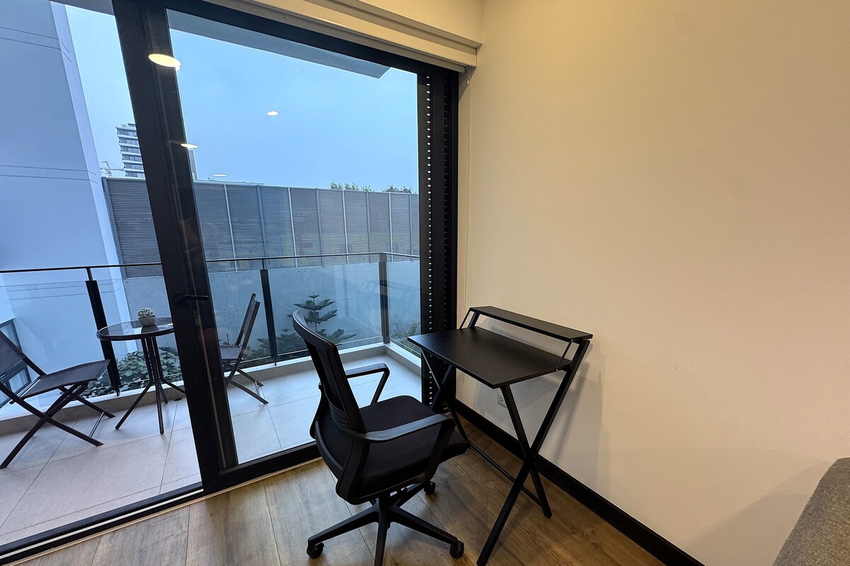 A modern room with a glass door leading to a balcony, a black office chair, a small round table, and a black desk.