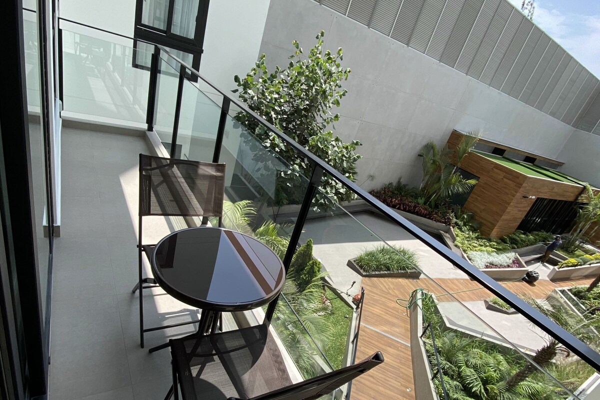 En moderne balkon med gelænder i glas, et spisebord med stole og udsigt til en anlagt have.